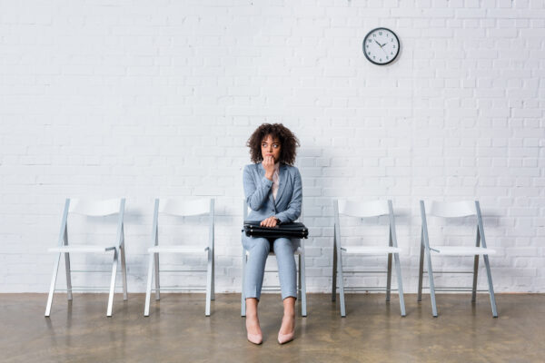 Stressed woman in suit sitting on chair with briefcase and waiting