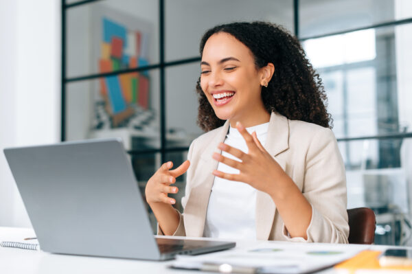 Excited emotional curly haired hispanic young business woman in stylish elegant clothes, team lead, business coach, talking by video conference with colleagues or partners on laptop, smile friendly